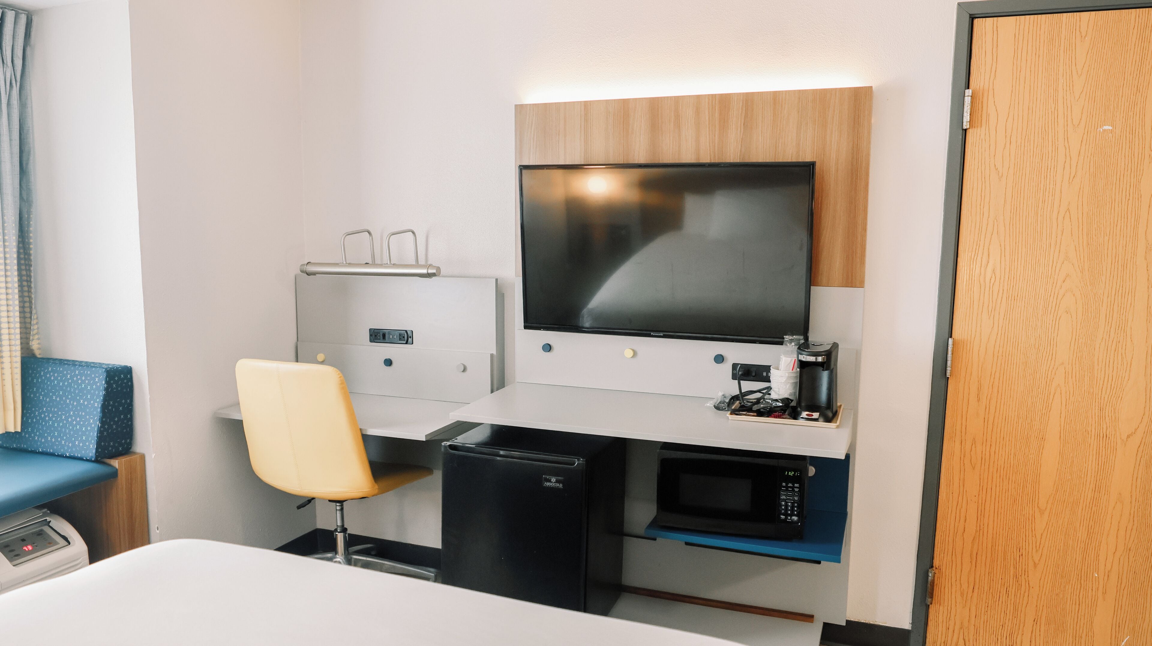 Une chambre d’hôtel équipée d’un lit, d’un bureau avec un ordinateur, d’une chaise, d’un petit réfrigérateur, d’un four à micro-ondes et d’une machine à café.