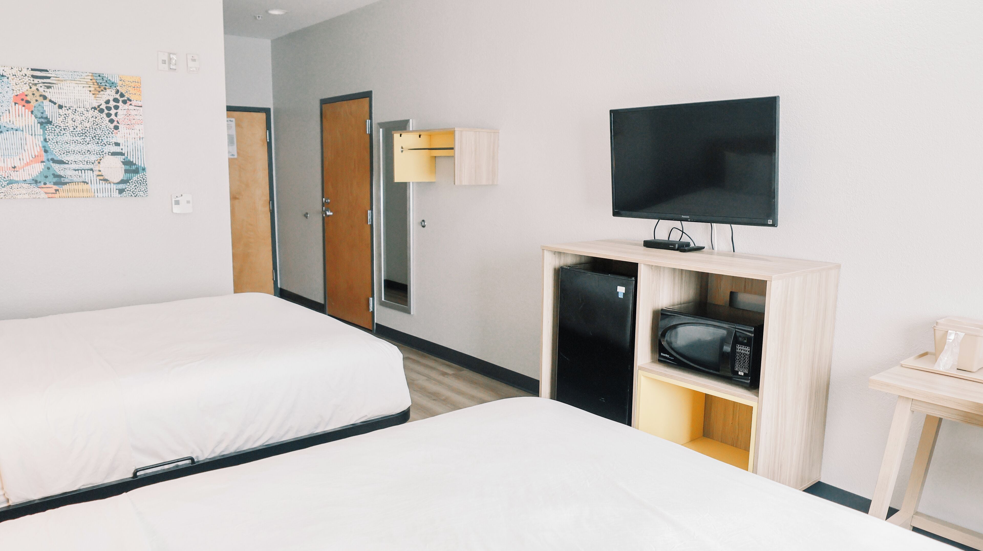Habitación de hotel con dos camas, televisión, microondas y una mesita.