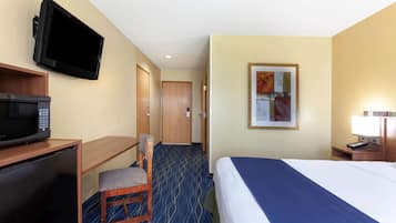 A hotel room with a bed, a desk with a microwave, a television mounted on the wall, and a framed picture on the wall.