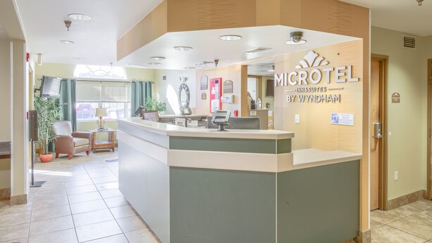 A reception area with a counter, a desk, and a chair. There are signs on the wall and a window with curtains. - Microtel Inn & Suites by Wyndham Gulf Shores (Gulf Shores)