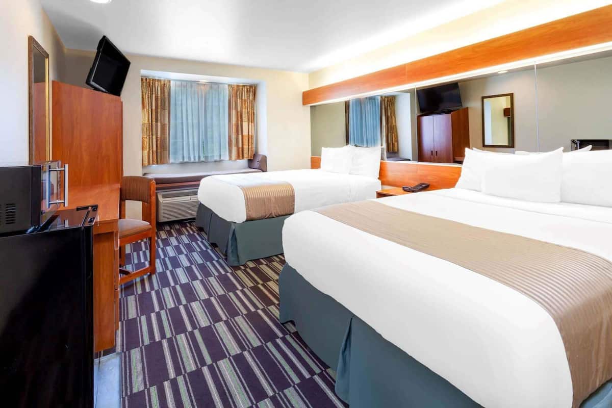 Ett hotellrum med två sängar, ett skrivbord, en TV och en sittgrupp med gardiner.