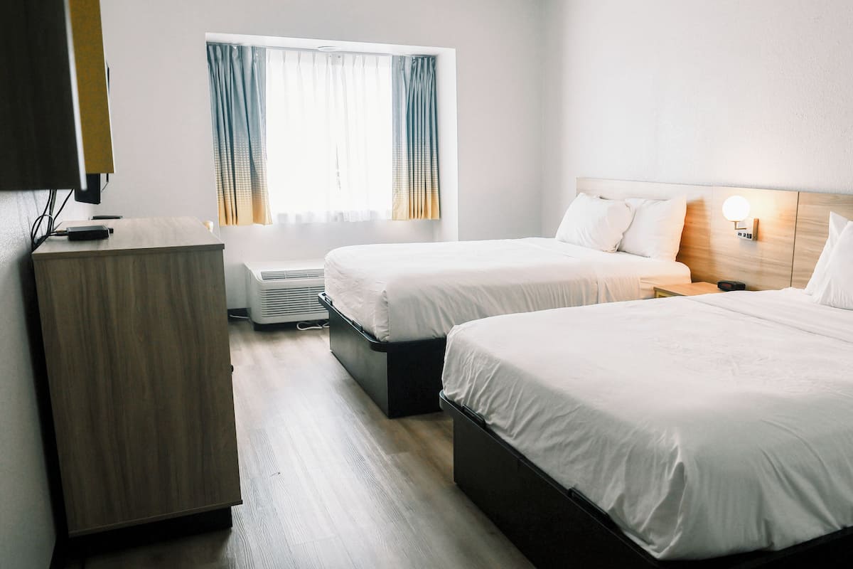 Ett hotellrum med två sängar, ett skrivbord och ett fönster med gardiner.