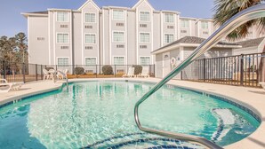 A swimming pool with clear water, surrounded by a fence and lounge chairs. - Microtel Inn & Suites by Wyndham Gulf Shores (Gulf Shores)