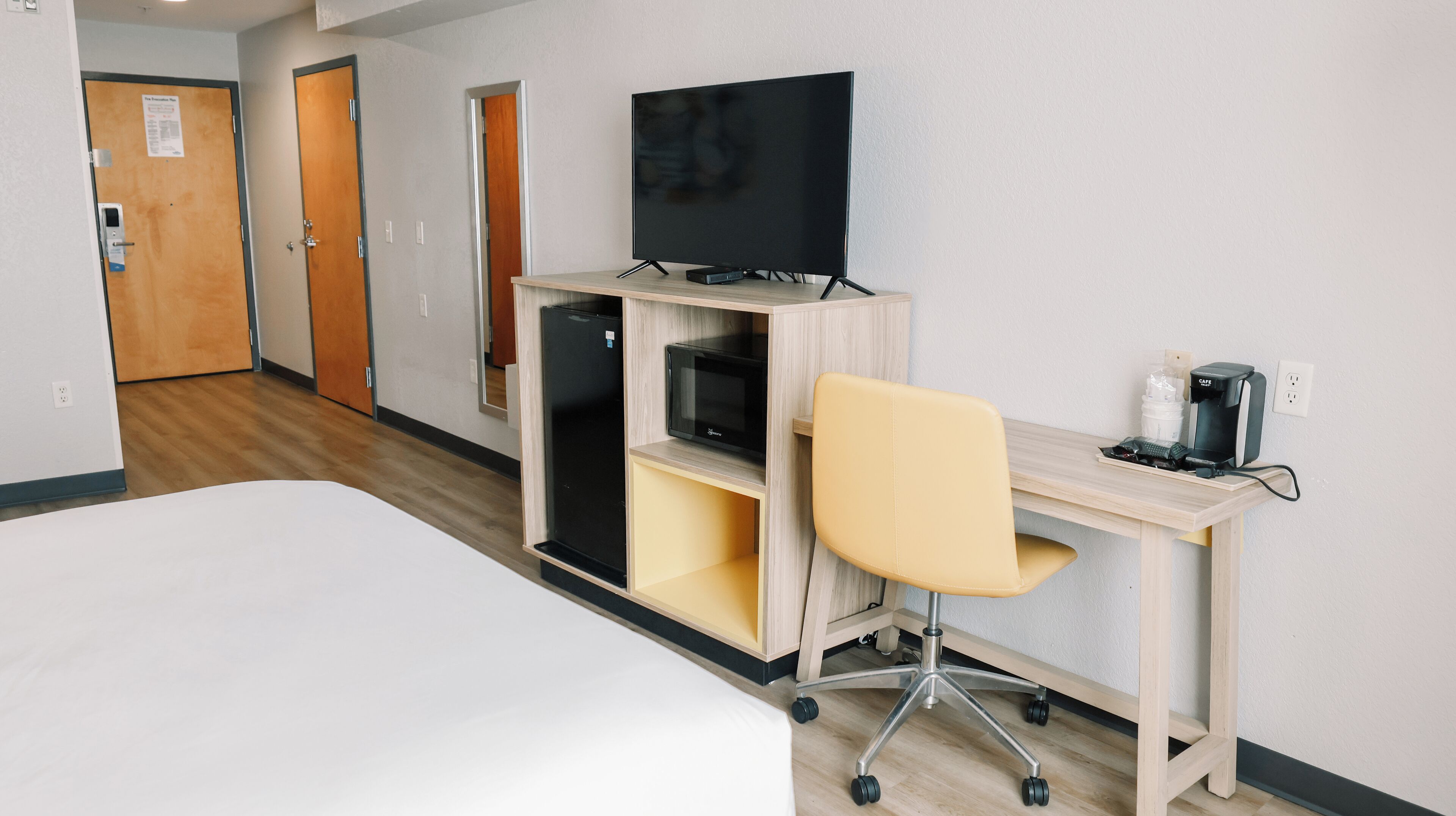 A hotel room with a bed, a desk with a computer, a TV, and a coffee maker.