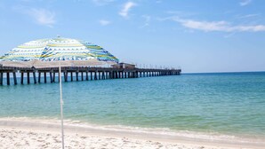 A beach with a striped umbrella and a pier extending into the water. - Microtel Inn & Suites by Wyndham Gulf Shores (Gulf Shores)