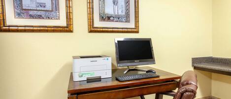 Mesa com impressora, monitor e teclado, uma cadeira de couro e duas molduras com imagens na parede.