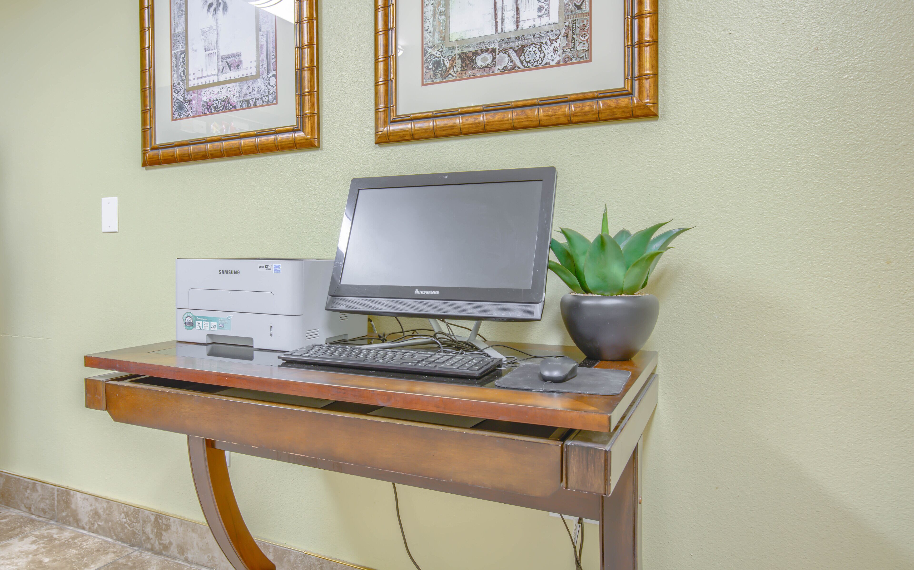 A computer desk with a desktop computer, keyboard, mouse, and a potted plant.