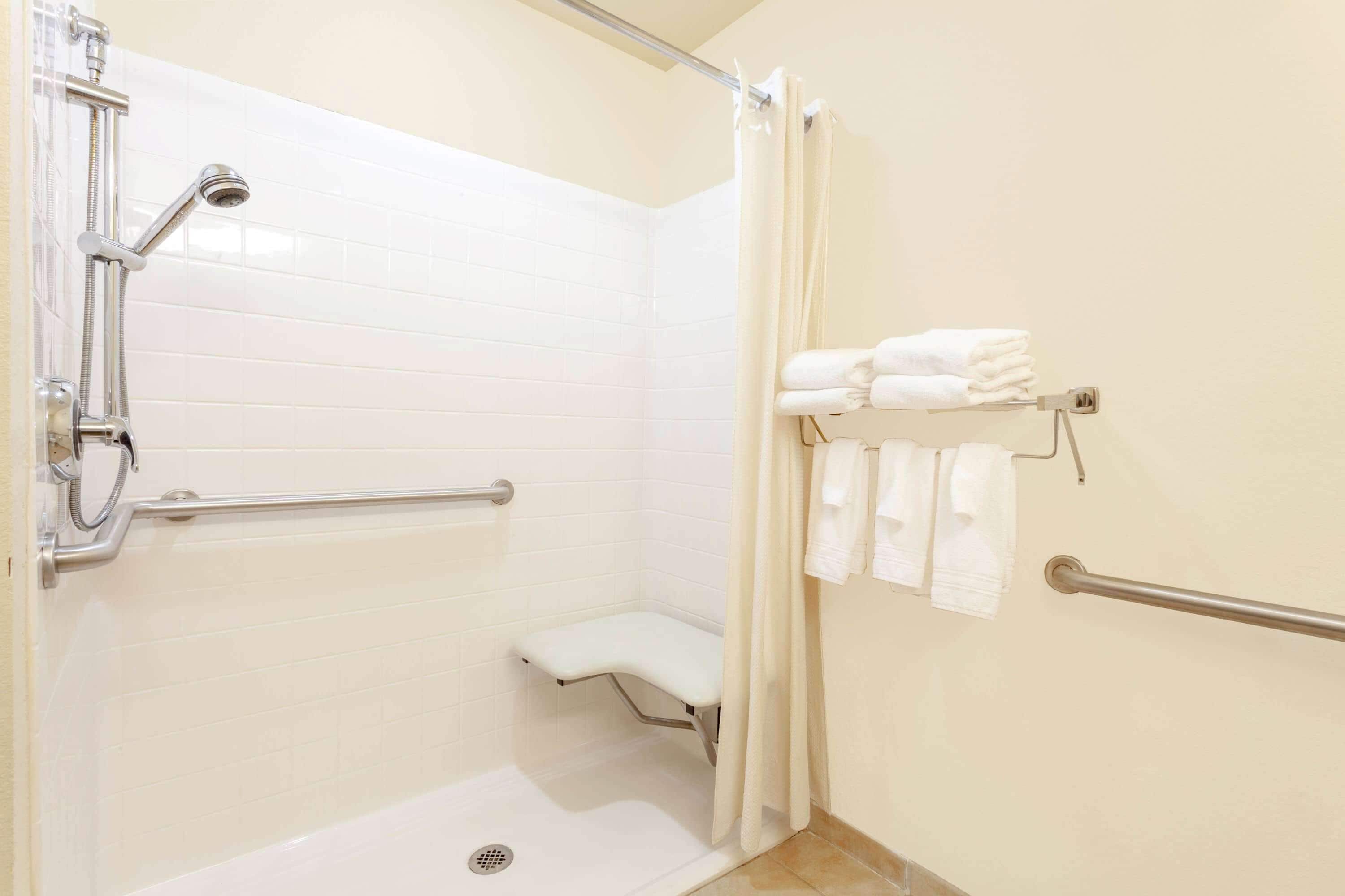A bathroom with a shower, grab bars, a bench, and a towel rack.