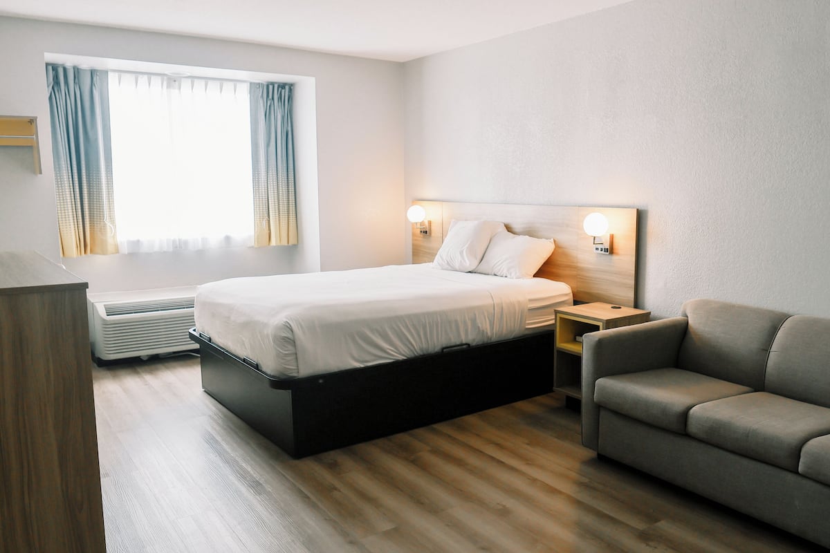 Ett hotellrum med en säng, en soffa, ett sängbord, en lampa och ett fönster med gardiner.