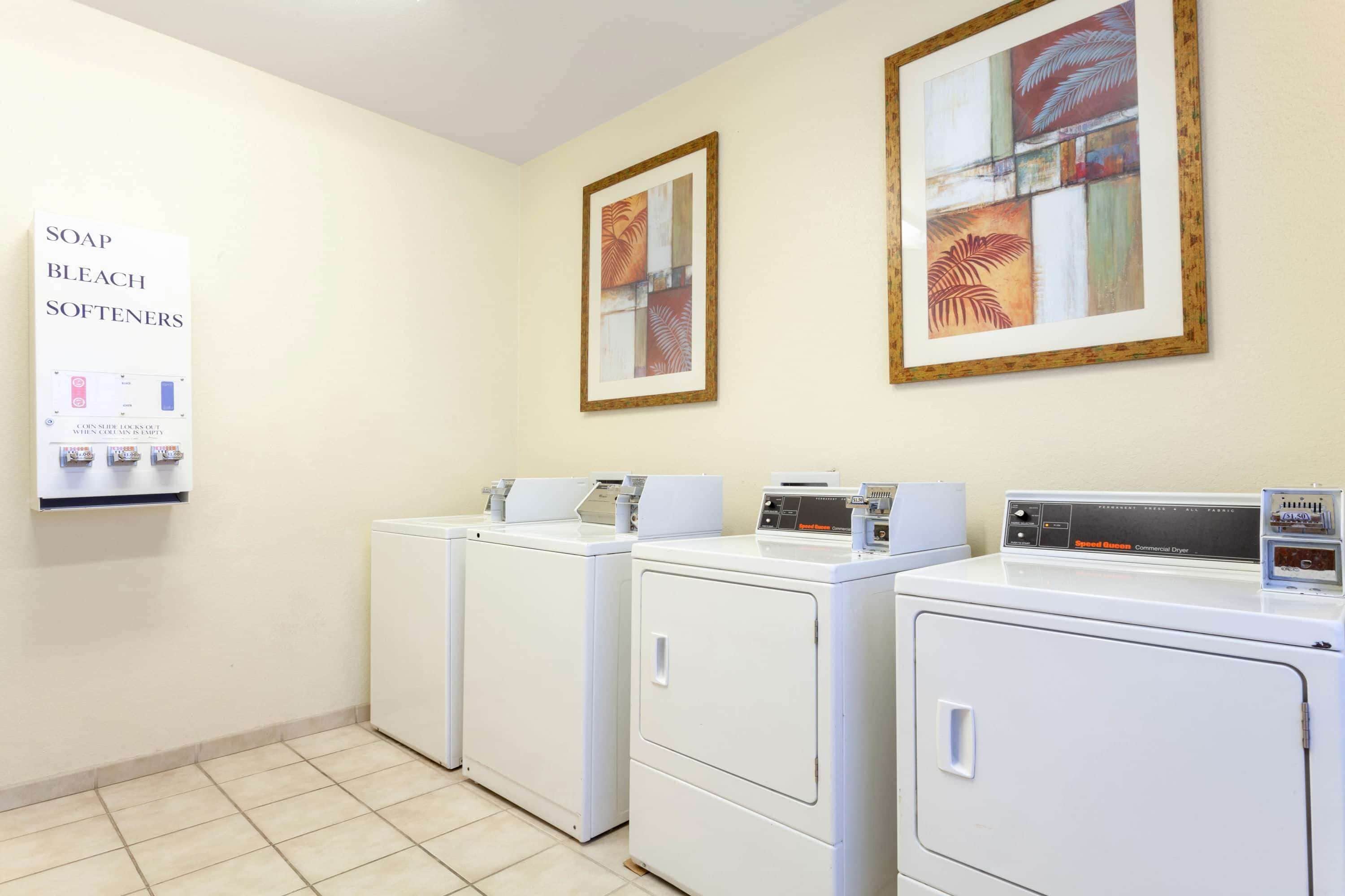 A laundry room with two front-loading washers and dryers, a sign about soap and bleach softeners, and framed artwork on the wall.