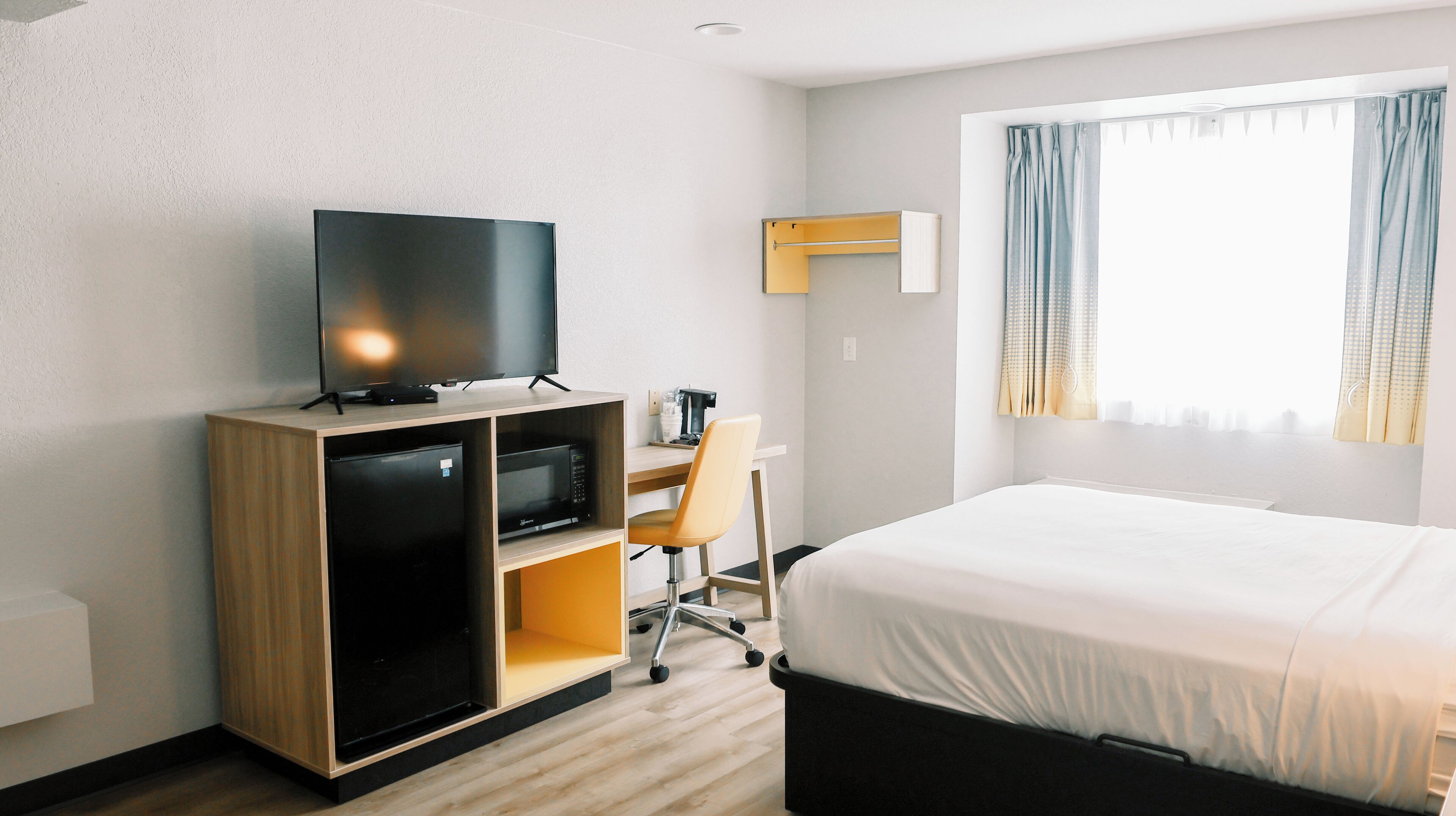 Une chambre d’hôtel comprenant un lit, un bureau avec une chaise, une télévision, une machine à café et une fenêtre avec des rideaux.