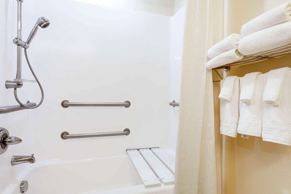 Un baño con bañera, barras de apoyo y un perchero para toallas.