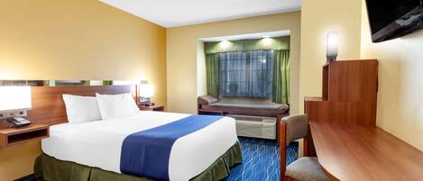 A hotel room with a bed, a desk, a chair, a television, and a window with curtains.