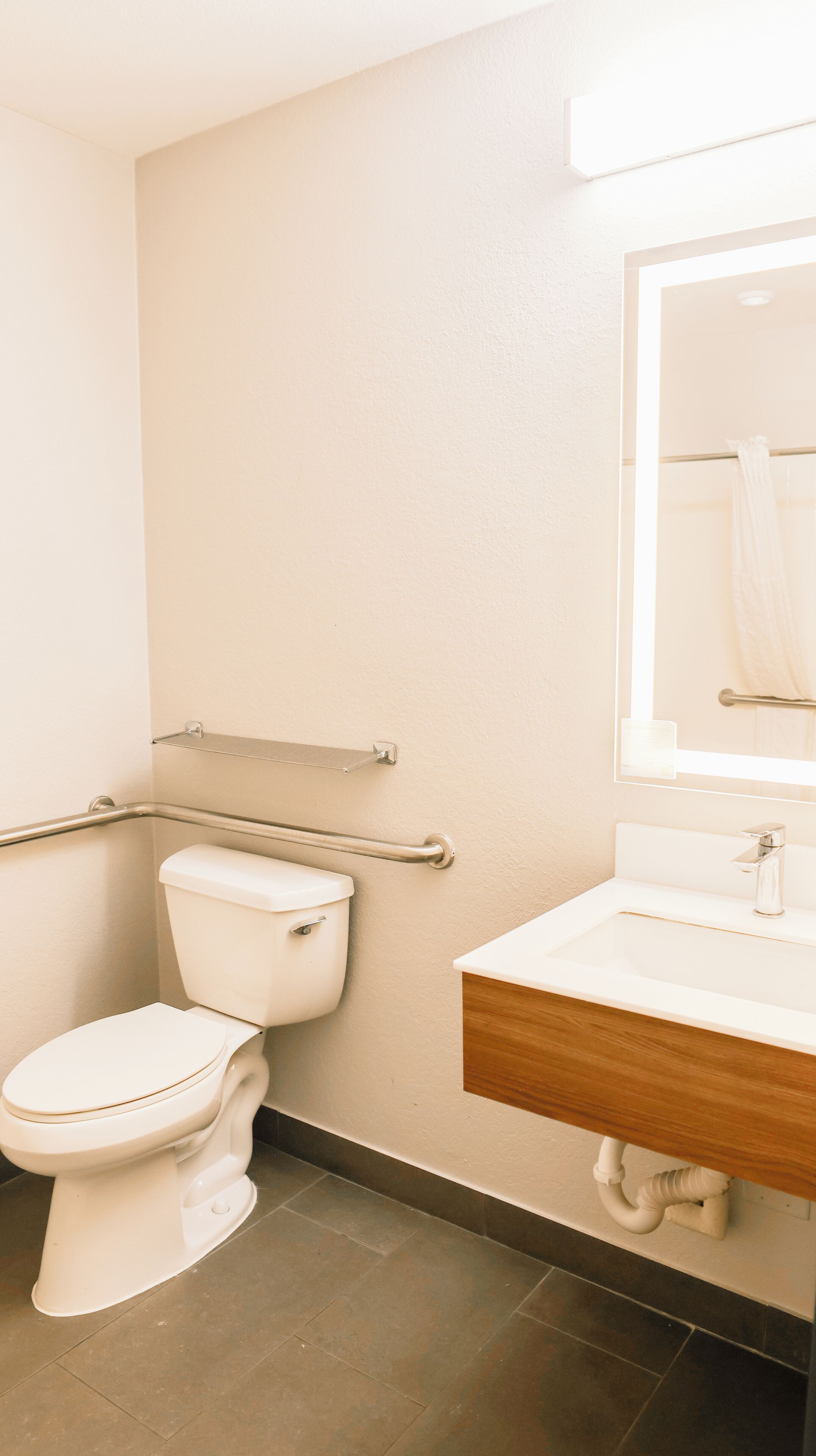 Een badkamer met toilet, wastafel, spiegel en een handgreep.