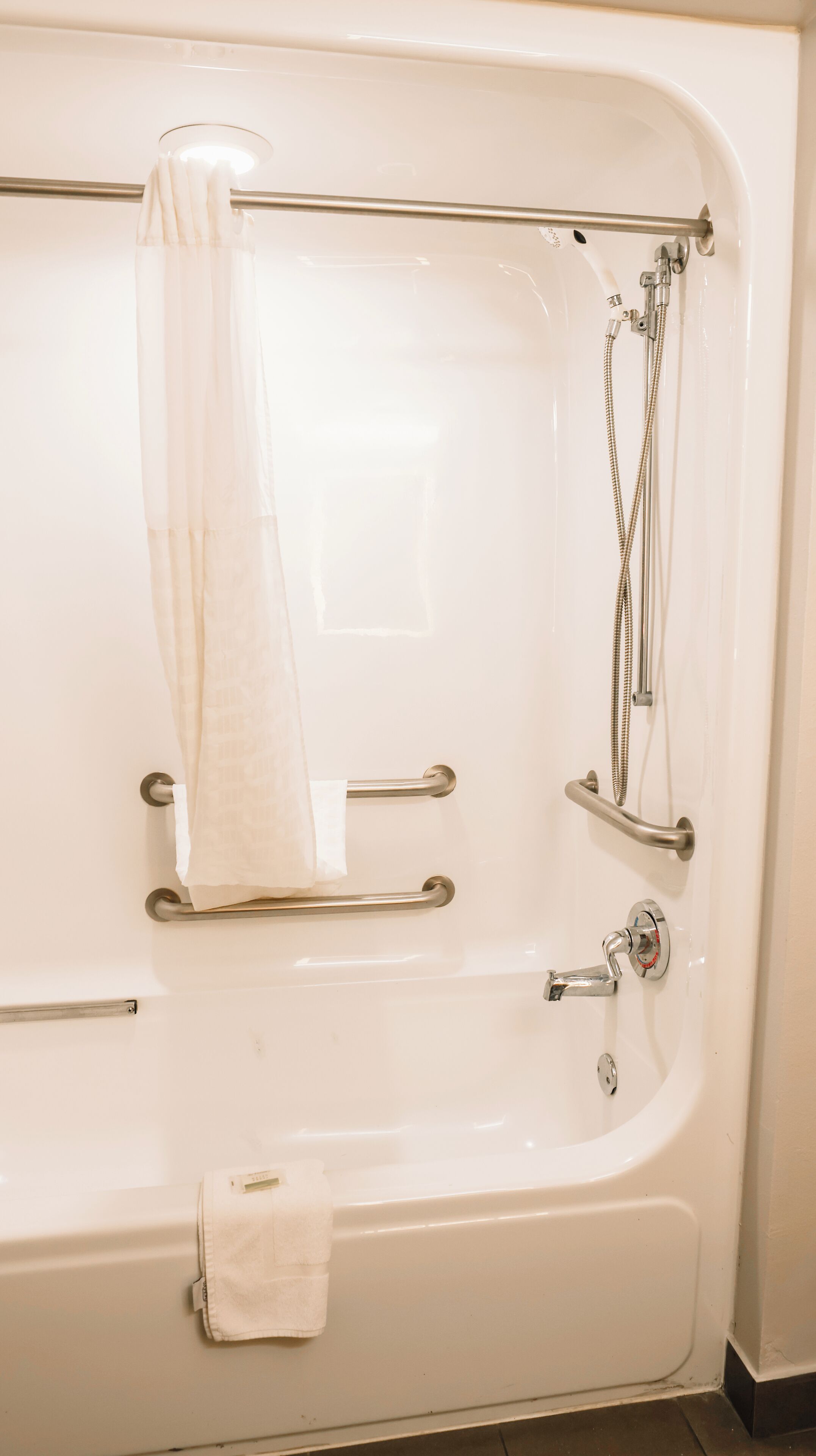 A bathroom with a bathtub, grab bars, a towel rack, and a showerhead.