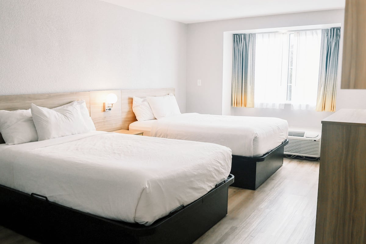 Ett hotellrum med två sängar, ett skrivbord och ett fönster med gardiner.