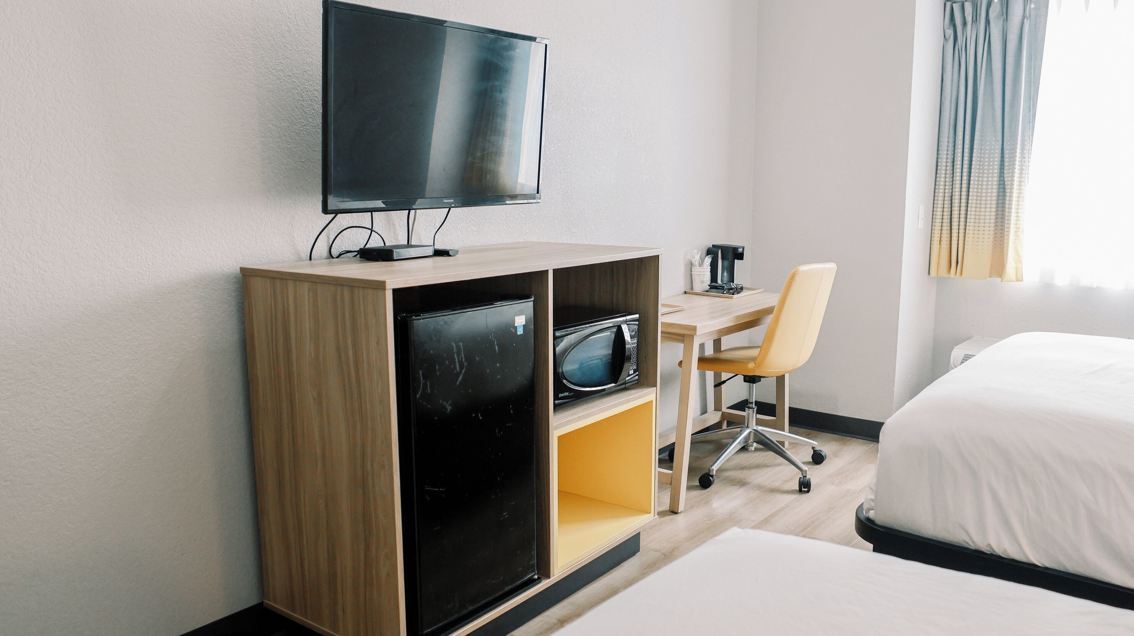Habitación de hotel con cama, escritorio con silla, televisión, microondas y refrigerador.