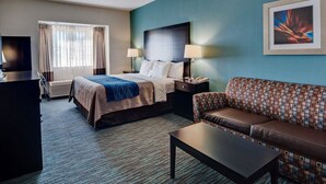 A hotel room with a bed, a sofa, a coffee table, a desk, and a TV.