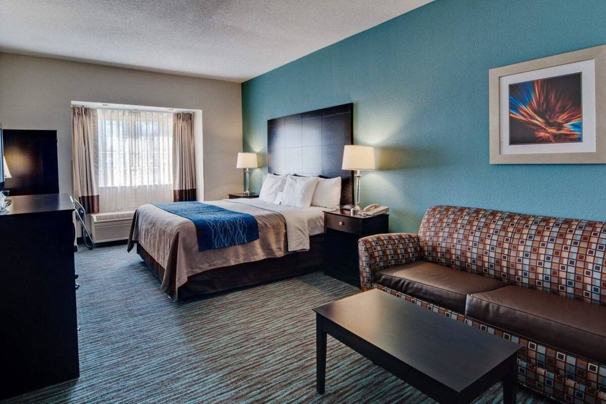 A hotel room with a bed, a sofa, a coffee table, a desk, and a TV.