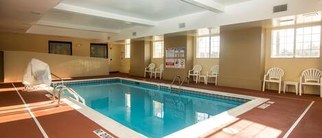 An indoor swimming pool with clear lane markings, safety signs, and white chairs around the perimeter.