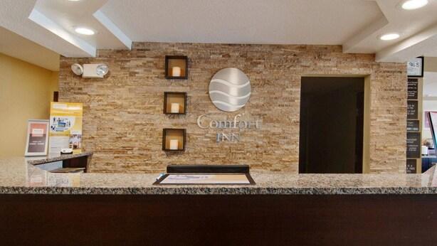 A hotel reception area with a stone wall, a reception desk, and a sign that reads "Comfort Inn".