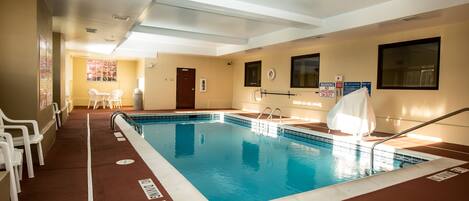 An indoor swimming pool with clear lane markings, a lifeguard stand, and a poolside area with chairs.