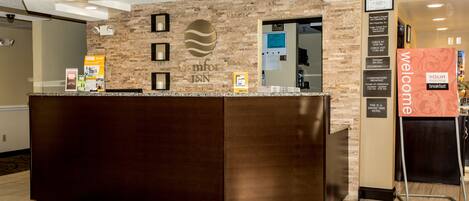 A reception desk with a stone facade, a framed sign above it, and a welcome banner to the right.