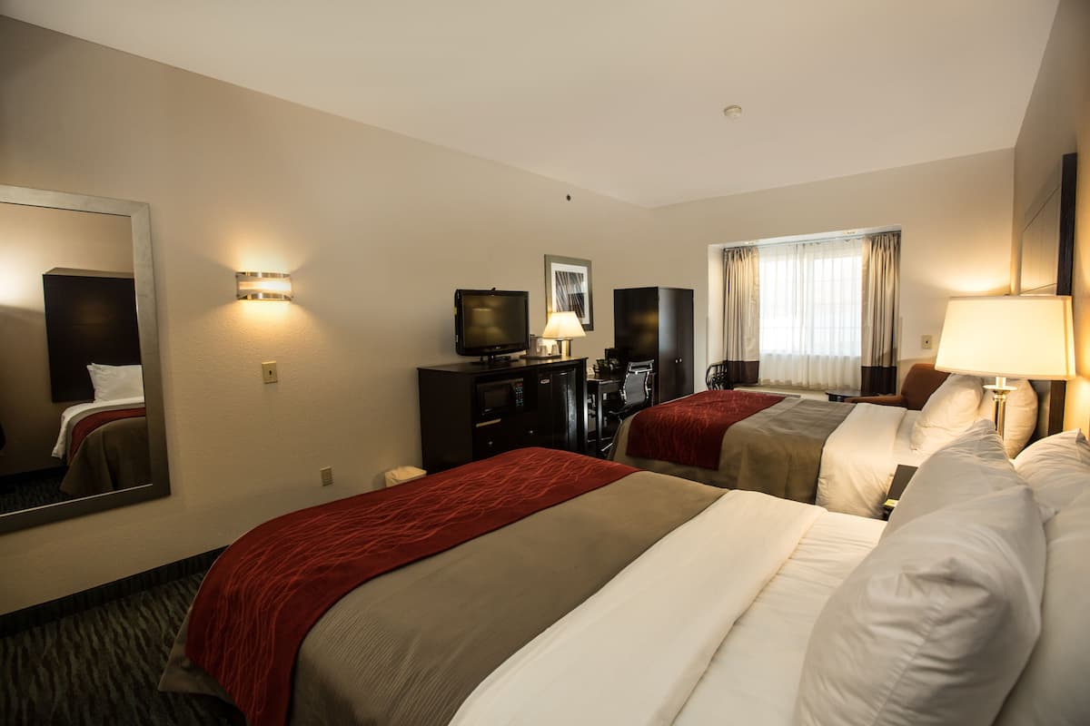 A hotel room with two beds, a television, a desk, and a large mirror.