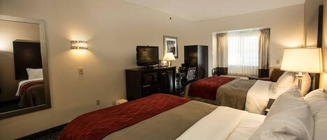 Habitación de hotel con dos camas, televisor, escritorio y un espejo grande.
