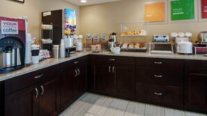 A hotel breakfast area with a coffee machine, juice dispenser, and various food items on display.