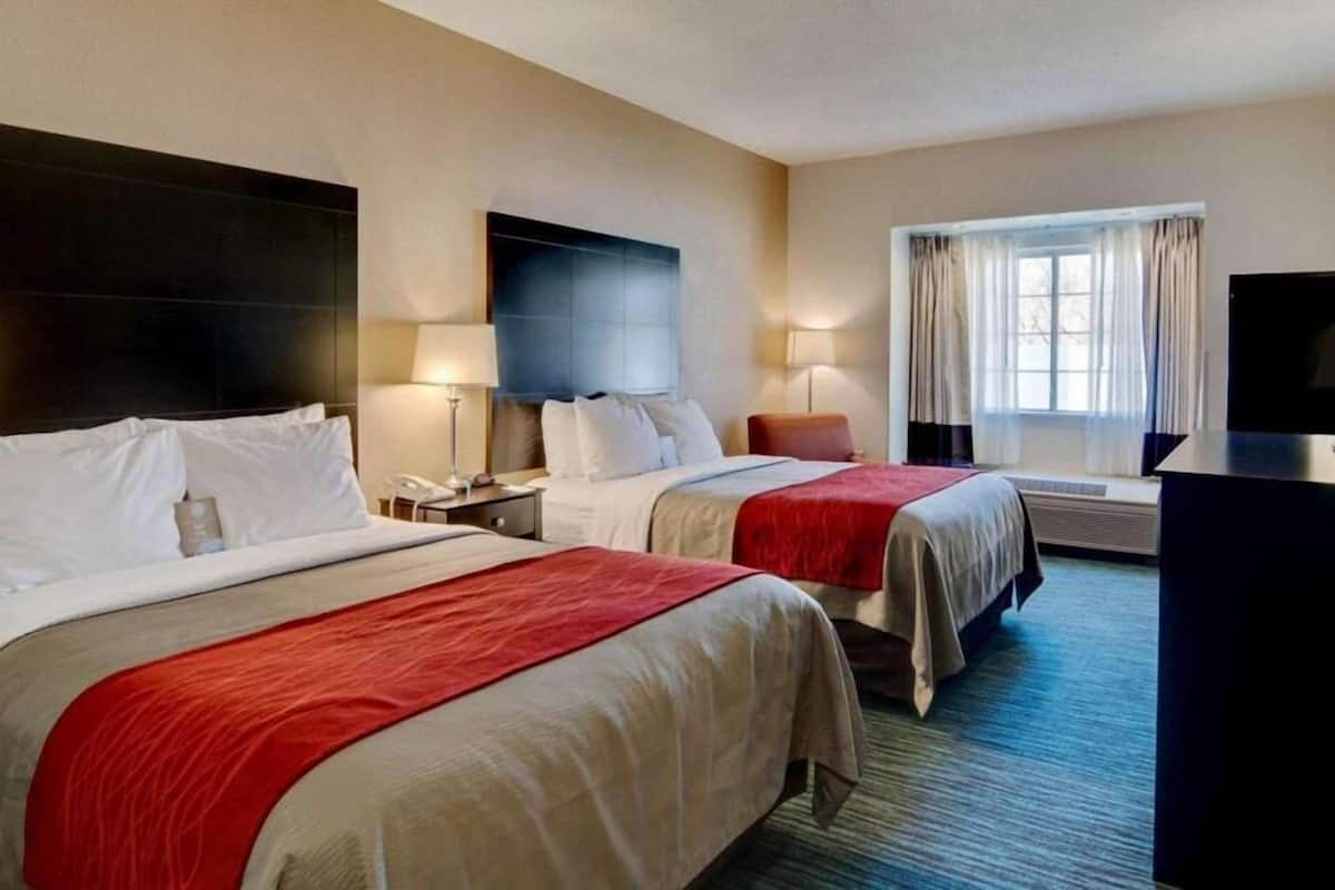 A hotel room with two beds, a flat-screen TV, a desk, and a window with curtains.