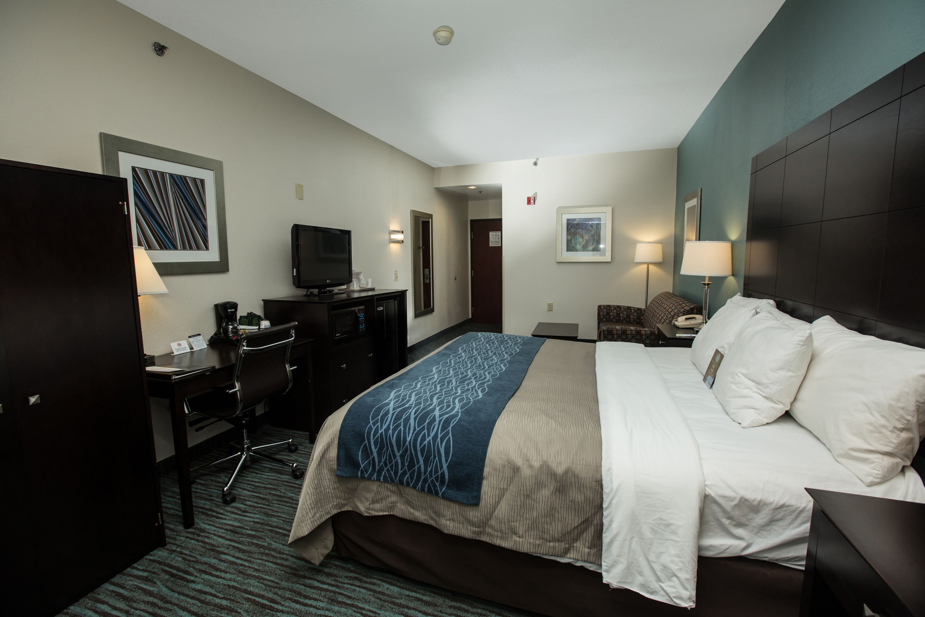 A hotel room with a bed, desk, chair, television, and artwork on the walls.