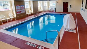 An indoor swimming pool with no diving signs, white chairs, and a red door.