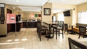 A hotel breakfast area with a counter, seating, and a TV mounted on the wall.