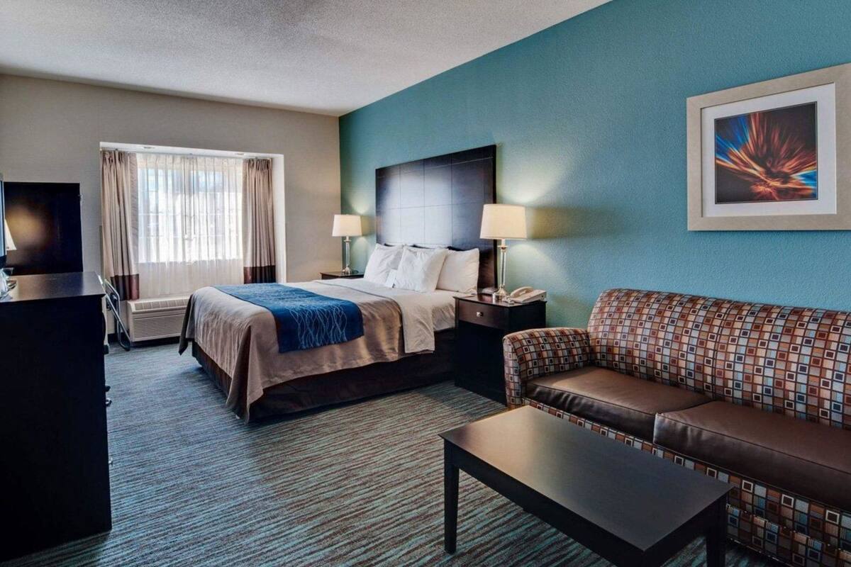A hotel room with a bed, a sofa, a coffee table, a desk, and a TV.