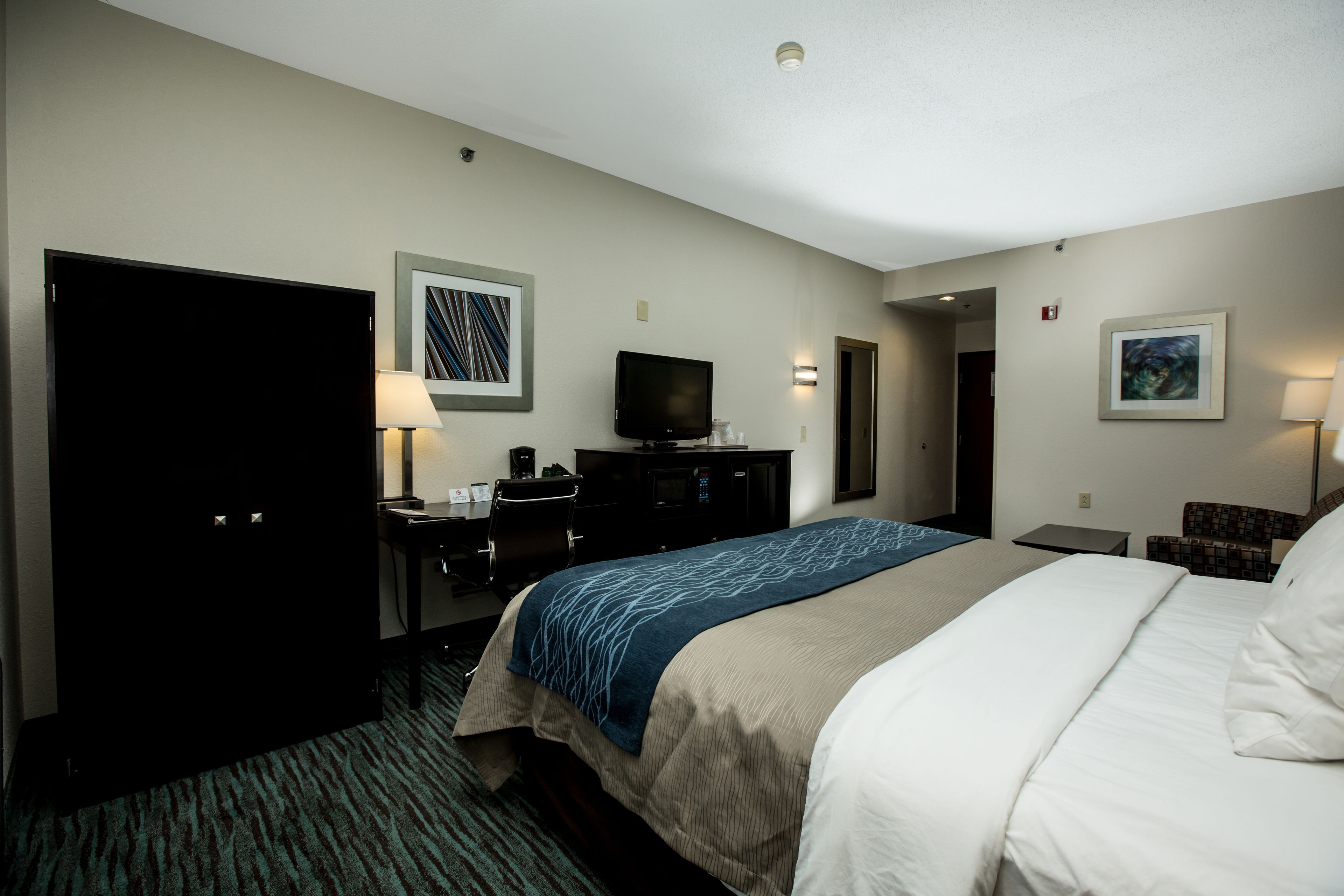 A hotel room with a bed, a desk, a television, and a door.