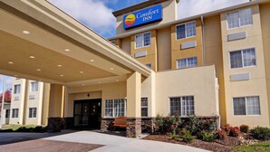 A Comfort Inn hotel with a covered entrance, multiple windows, and a landscaped area with a bench.