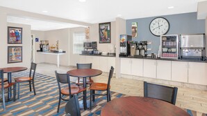 Un vestíbulo de hotel con zona de cocina, mesas de comedor, sillas y un reloj en la pared.