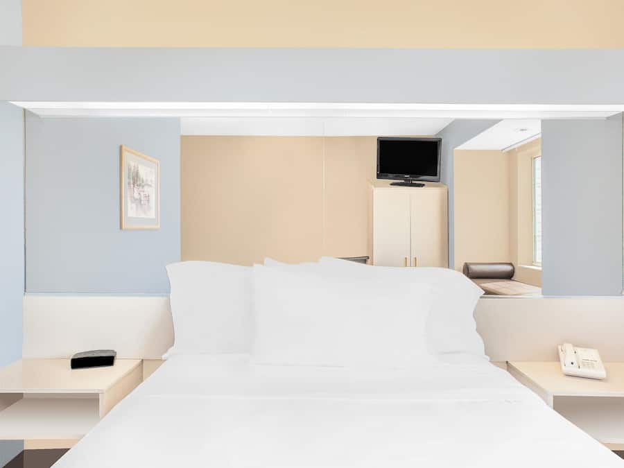 Ett modernt hotellrum med en säng, sängbord, en tv och en telefon.