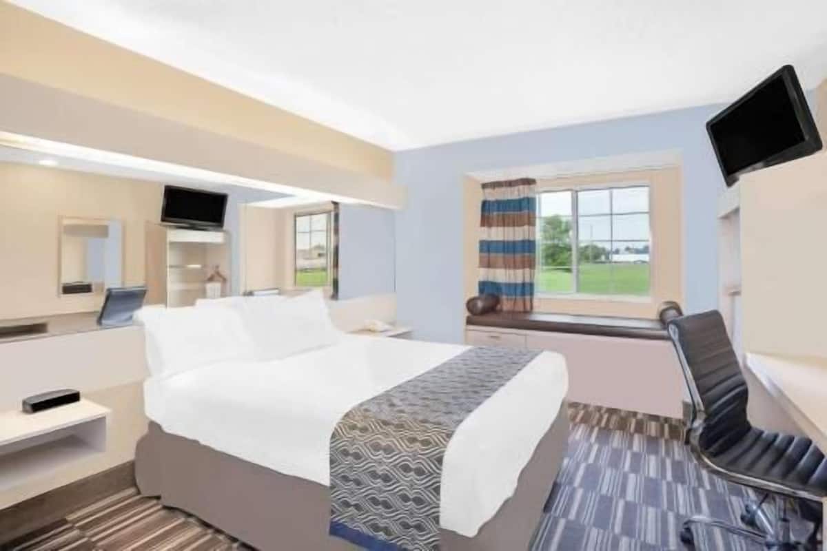 A hotel room with a bed, a desk, a chair, a TV, and a window with curtains.