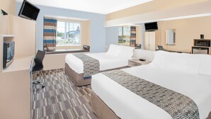Habitación de hotel con dos camas, un televisor montado en la pared, un escritorio y una ventana con cortinas.