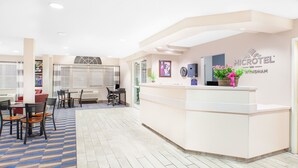 Un área de recepción con un mostrador blanco, un reloj y un letrero del Microtel Inn Whidham. Hay sillas y mesas dispuestas para los huéspedes.