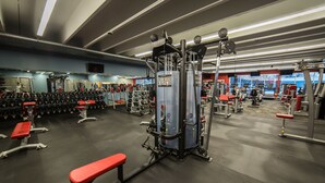 Un gimnasio con diverso equipo de ejercicio, bancos y estantes para pesas.