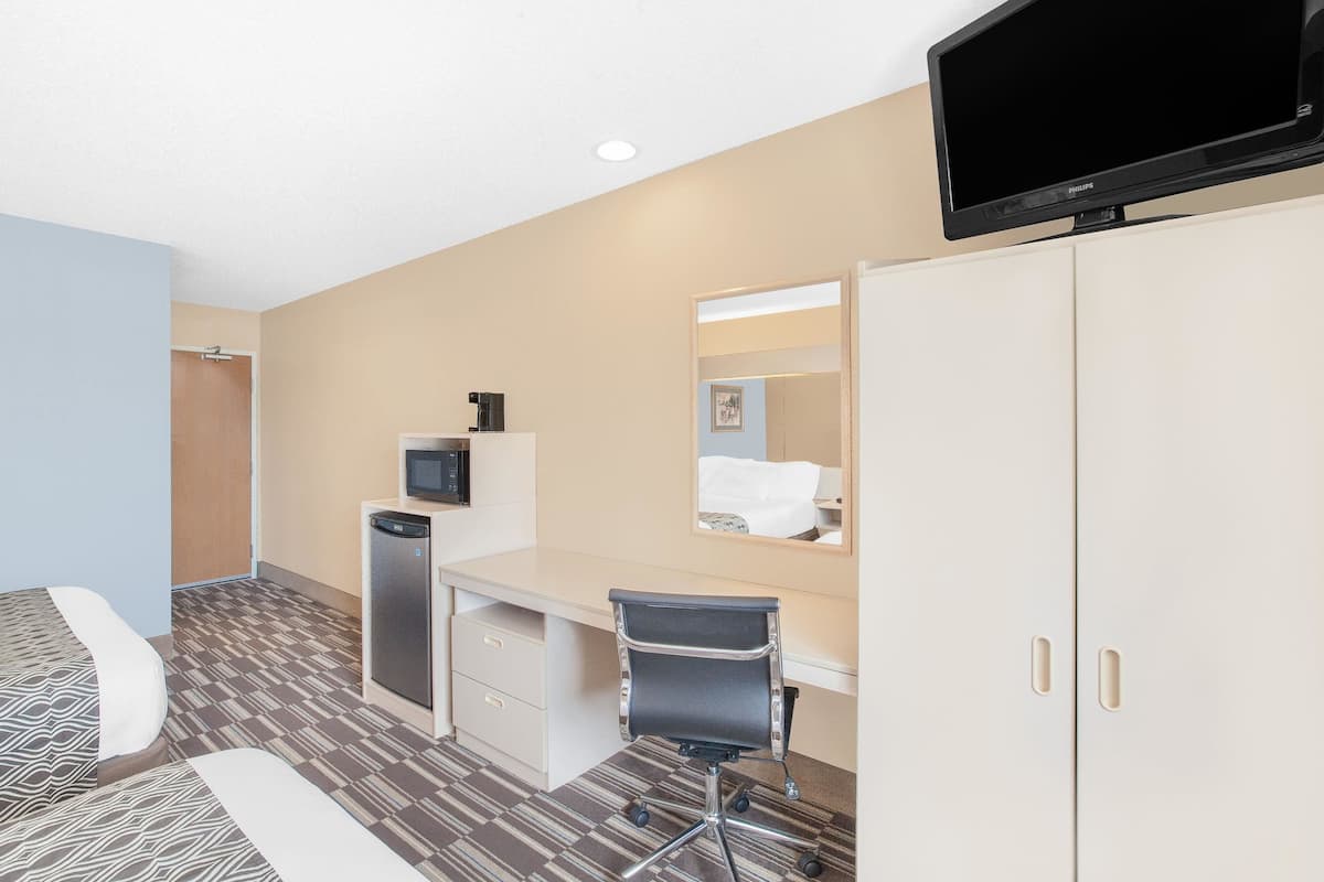 A hotel room with a bed, a desk, a chair, a television, a mirror, and a wardrobe.