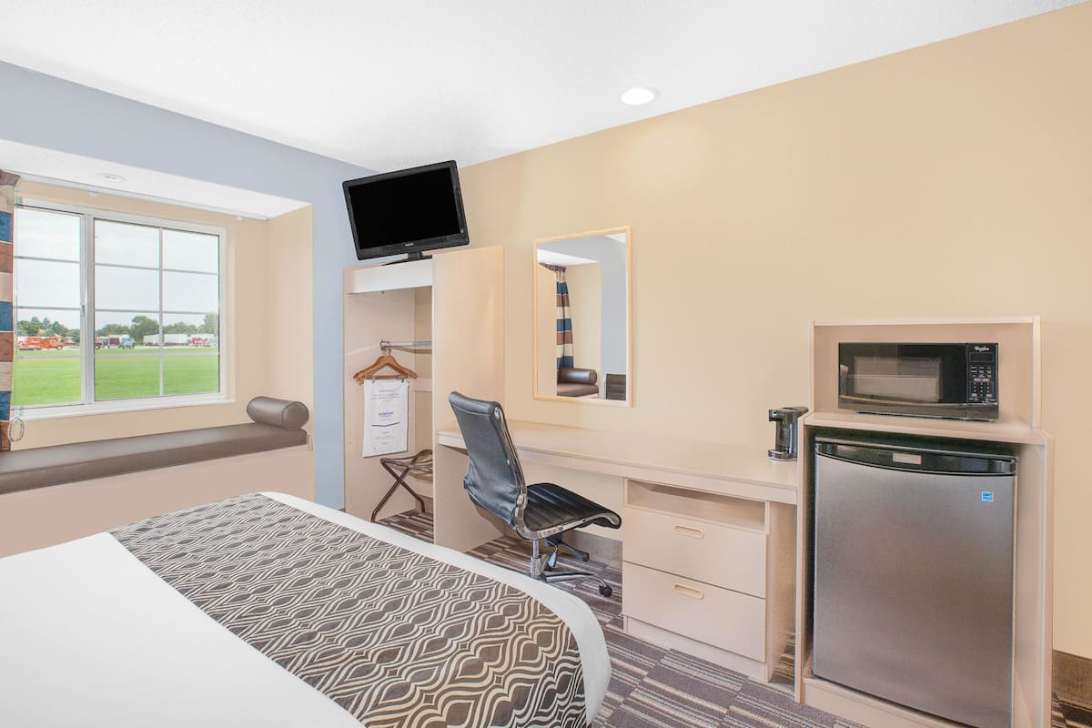 A hotel room with a bed, a desk with a chair, a television, a microwave, and a refrigerator.