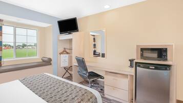 Habitación de hotel con cama, escritorio y silla, televisión, microondas y refrigerador.