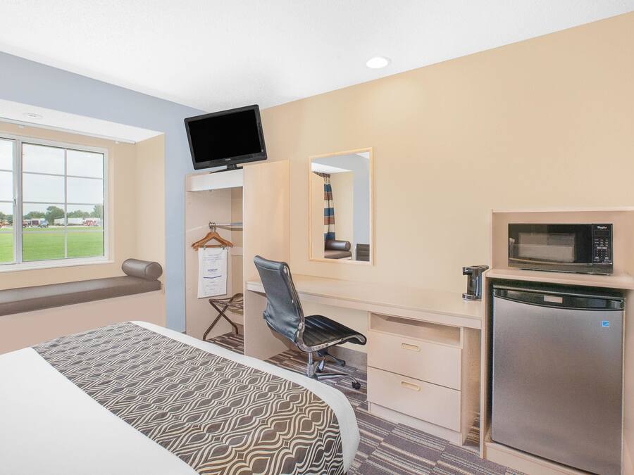 Habitación de hotel con cama, escritorio y silla, televisión, microondas y refrigerador.
