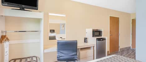 Habitación de hotel con cama, escritorio, silla, televisión, microondas y refrigerador pequeño.