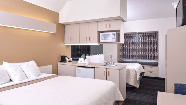 A hotel room with a bed, a desk, a microwave, and a window with curtains.