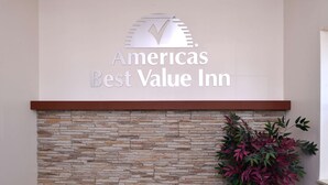 A sign for Americas Best Value Inn with a stone wall and a potted plant.